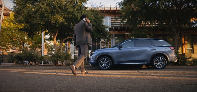 Man on a phone passing by an INFINITI suv